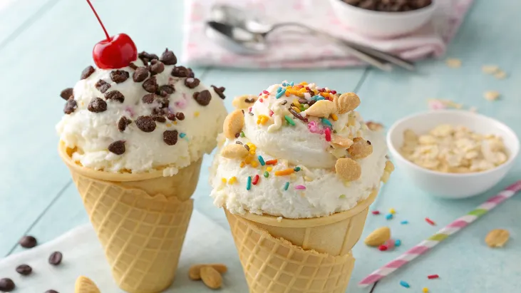 Two cones of cottage cheese ice cream with chocolate chips, sprinkles, and a cherry on top.